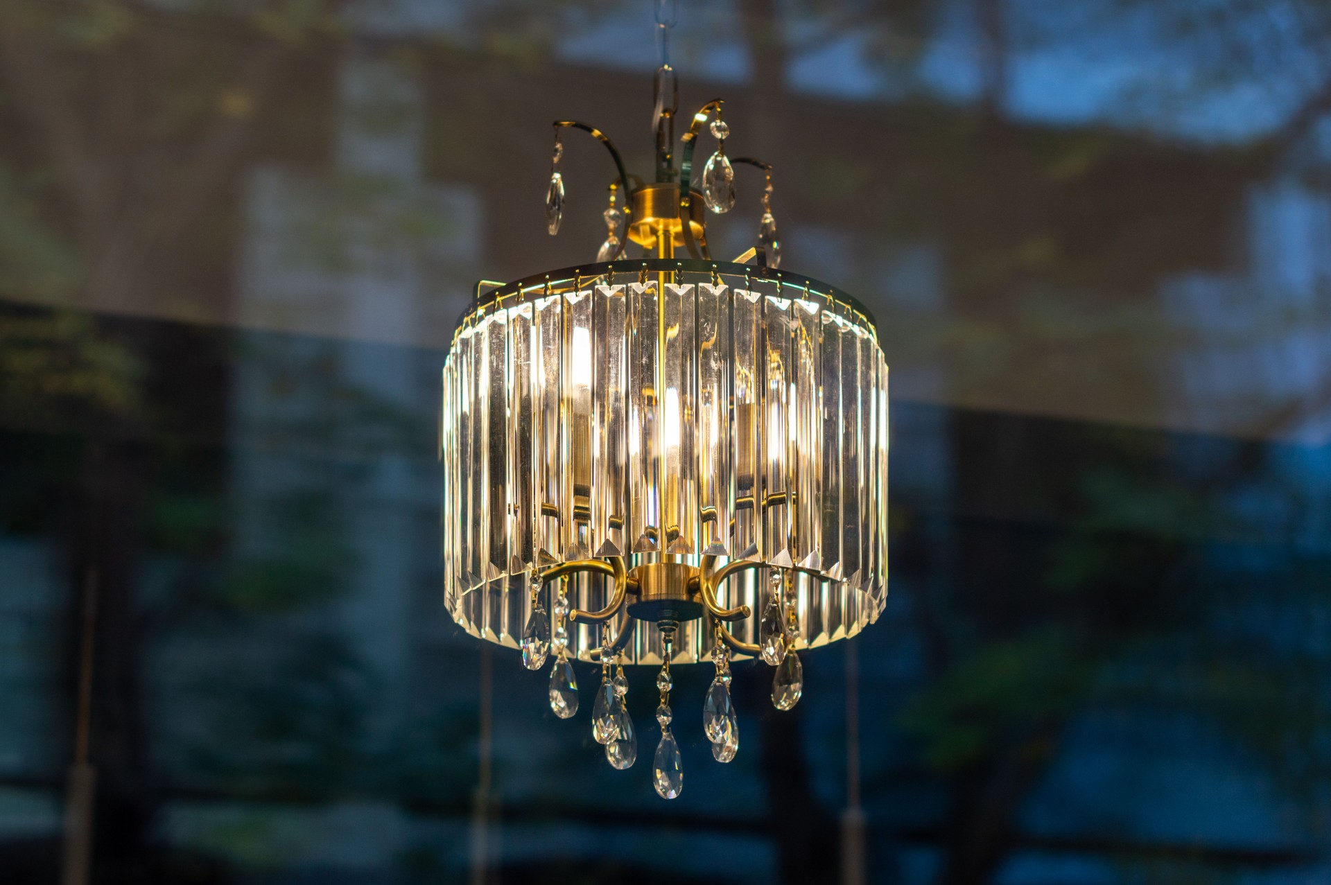 Lit crystal chandelier hanging on the ceiling behind the house window glass, view from outdoors.